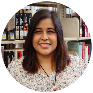 A young woman with brown hair standing in front of a shelf of books